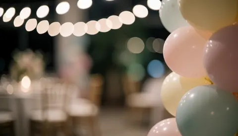 Close-up column of pastel balloons with blurred warm lights and event tables in the background, suitable for advertising text