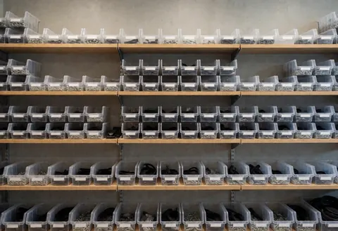 Transparent boxes of cell phone repair parts organized on wooden shelves in a concrete-walled storage area with good lighting