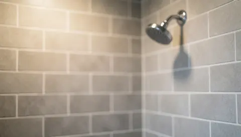 Close-up of a gray tiled shower corner with white grout lines, chrome showerhead, and warm diffused lighting suitable for bathroom installation text backgrounds