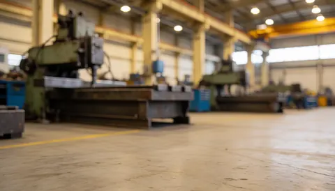 Out of focus industrial workshop featuring metal machinery, concrete pillars, and a concrete floor with warm lighting, suitable for service text overlays.