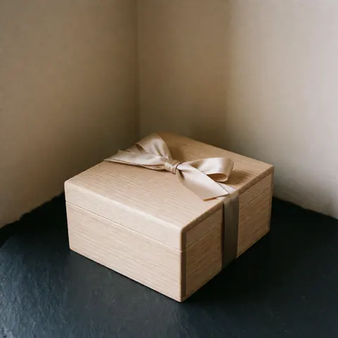 A wooden gift box tied with a beige ribbon sits in the corner on a dark surface against a beige wall with soft natural lighting