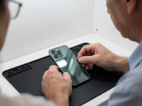 Close-up of technician hands inspecting a mobile phone with a green back panel on a workbench.
