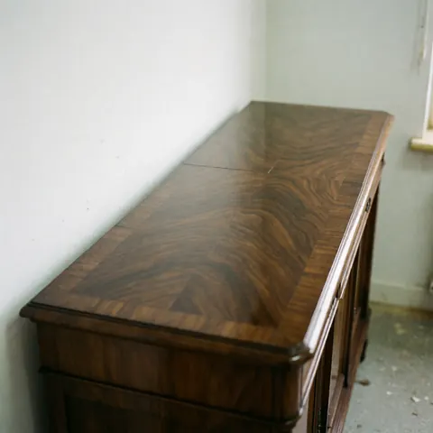 Antique dark wood furniture with a glossy finish reflecting light against white walls and a dusty floor