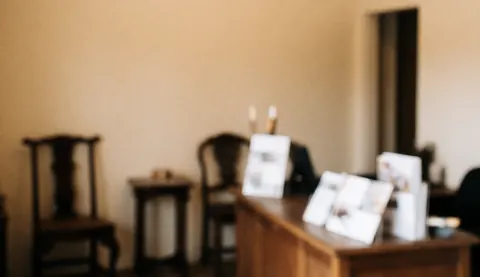 Reception area of an antique furniture restoration workshop featuring wooden tables and chairs, beige walls, and brochures on a wooden table.