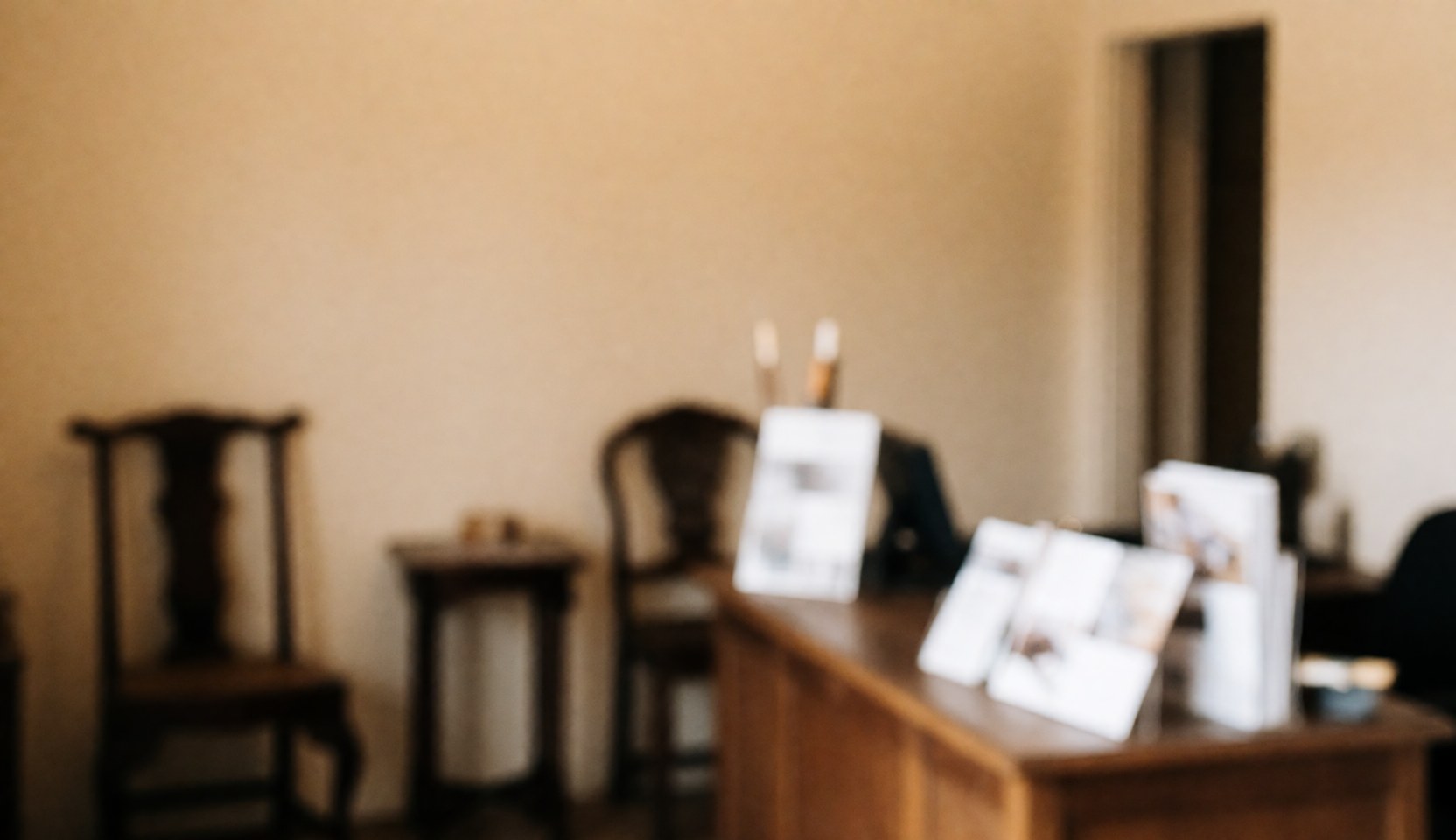 Reception area of an antique furniture restoration workshop featuring wooden tables and chairs, beige walls, and brochures on a wooden table.