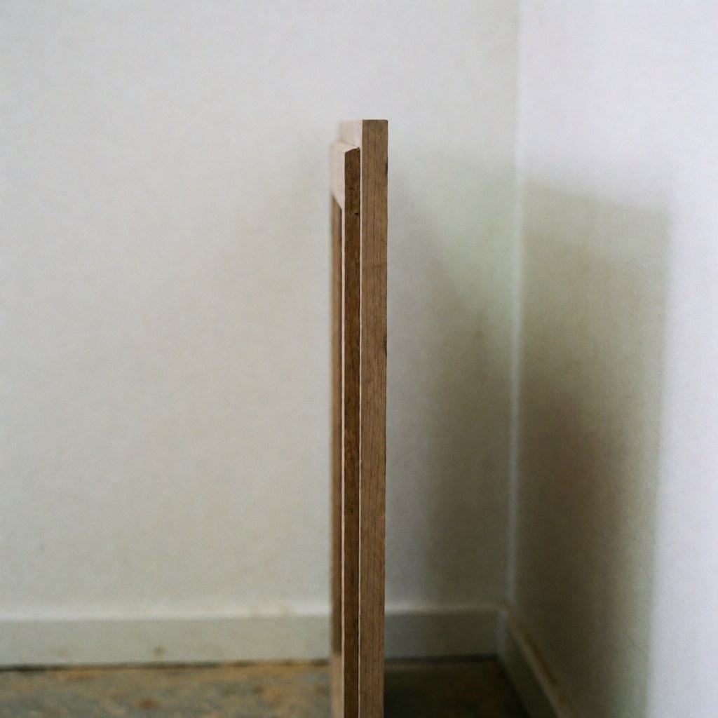 Side view of a restored antique cabinet door showing precise joinery between new and old wood against a white wall with soft ambient light highlighting the texture.