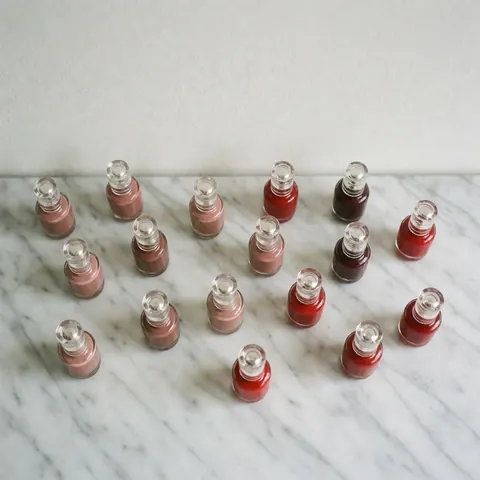 Top-down view of nude and red nail polish bottles arranged on a white marble surface for a manicure catalog