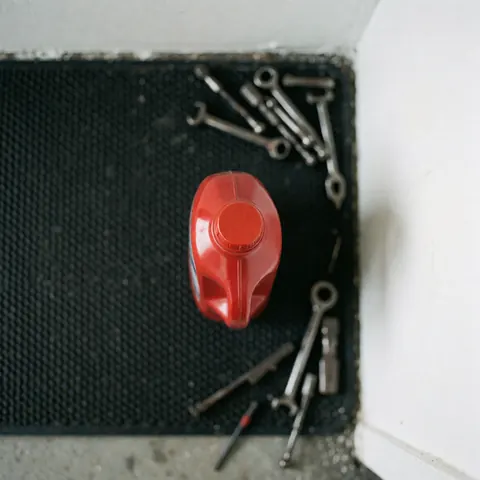 Top view of a red oil bottle on a black mat surrounded by scattered wrenches in a mechanic shop setting