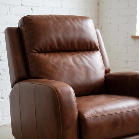 Restored brown leather chair with visible stitching and rich texture in a workshop with a white brick wall.