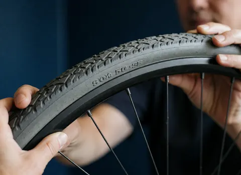 Close-up of hands adjusting a bicycle tire, showing tread pattern and specifications against a deep blue wall