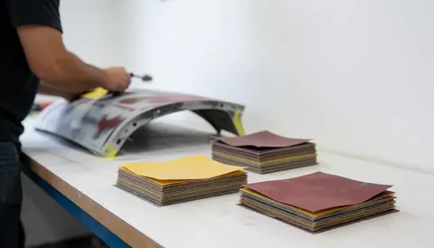 Close-up of hands using sandpaper on a car body in a well-lit workshop during the restoration process