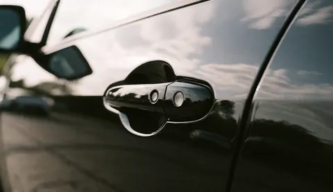 Close-up of a black car door with flawless glossy paint reflecting the sky, showcasing high-quality automotive bodywork and finish.