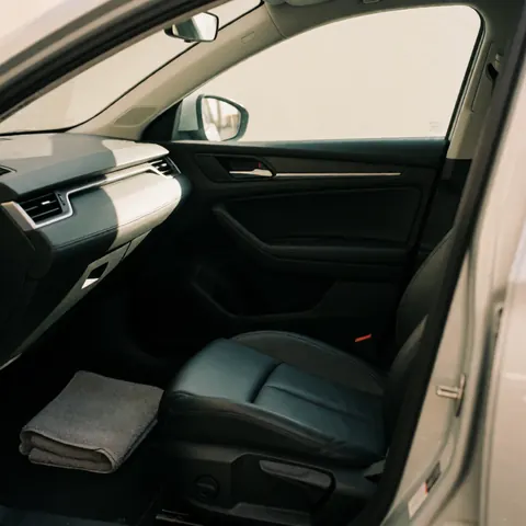 Close-up of a modern black leather car seat with subtle stitching, a folded gray towel on the floor, and sunlight illuminating the dashboard.