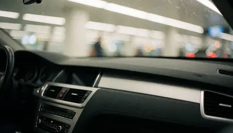 Blurred airport lights visible through a car windshield behind the dashboard, creating a calm and safe background for text overlays.