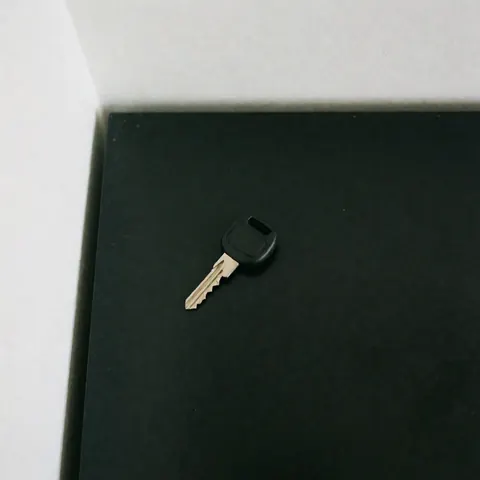 Black car key with metal teeth on a clean black surface, softly lit for service catalogs