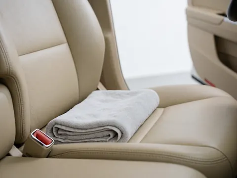 A folded gray towel rests on a beige leather car seat with a visible seatbelt, highlighting interior cleanliness and comfort.