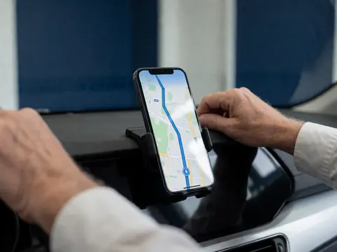 Close-up of hands adjusting a smartphone in a car mount, displaying a blue navigation route on the screen inside the vehicle interior.
