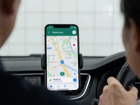Mobile phone mounted on a car dashboard displaying a navigation map while the driver's hands rest on the steering wheel.