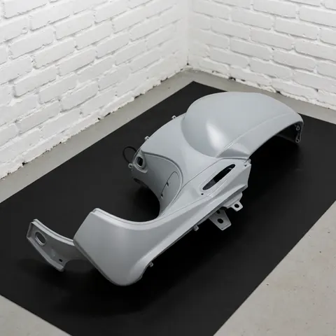 Gray painted scooter body panel resting on a black mat with a white brick wall background and professional lighting