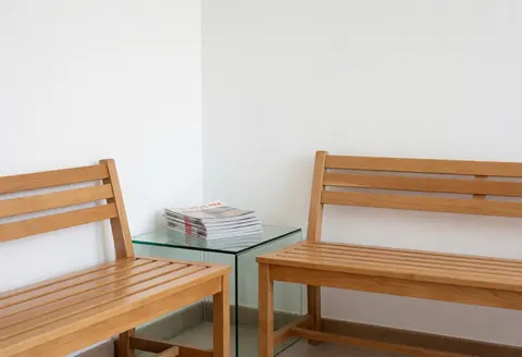 Clean modern waiting room with two wooden benches and a glass table holding magazines against white walls