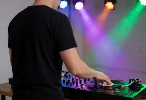 A DJ mixing music on a console with stage lights in the background and gray walls creating a party atmosphere.