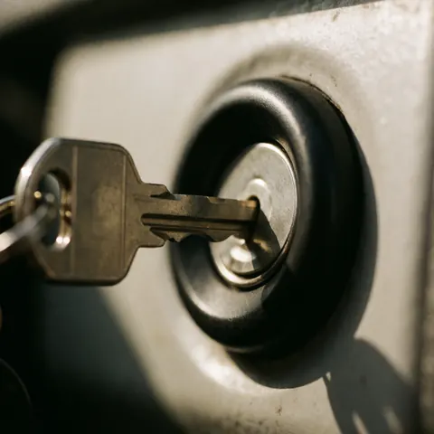 Close-up of a metal car key inserted into a vehicle's ignition lock, highlighting the teeth and black plastic texture with warm lighting and a blurred background.
