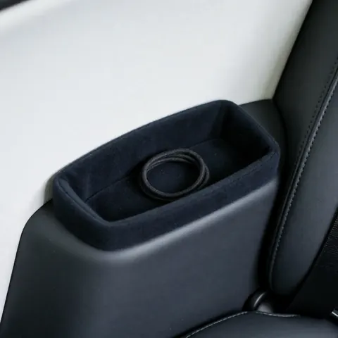 Close-up of a black cushion with an elastic hair tie placed on a taxi seat against a clean white wall