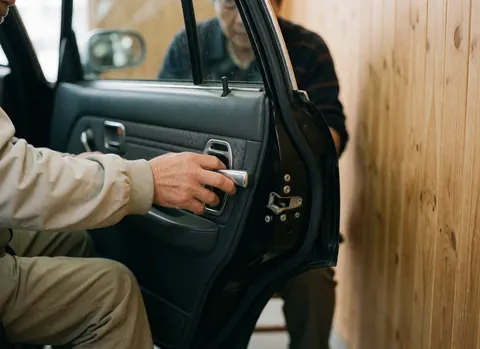 Close-up of an adult hand adjusting the door mechanism of a taxi against a natural wood wall background.