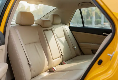 Clean beige rear seats in a yellow taxi with visible seat belts and natural light entering through the windows.