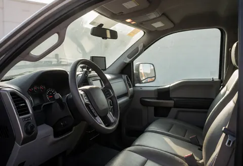 Bright interior of a clean pickup truck featuring a steering wheel, dashboard, and leather seats with sunlight streaming through the windshield.