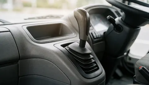 Close-up of a truck gear shift featuring a metal handle, textured plastic console, and diffused natural lighting, suitable for commercial text backgrounds.
