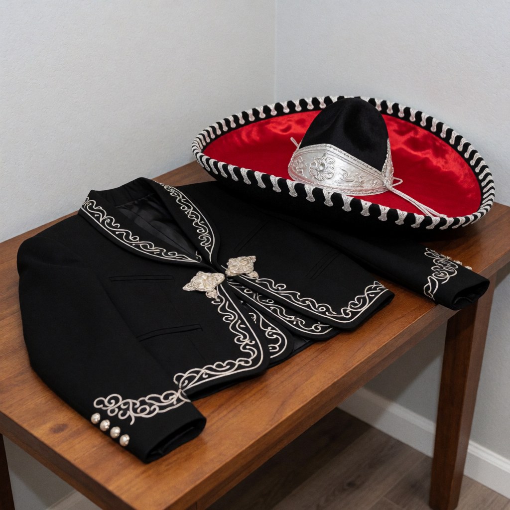 Black charro suit with silver embroidery and hat with red lining on a wooden table, ideal for events.