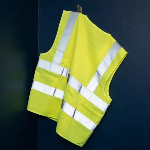 Yellow safety vest with reflective stripes hanging on a navy blue wall, illuminated by warm light highlighting its texture and details