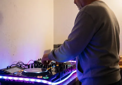 Professional DJ mixing music on a controller with blue and purple neon lights and warm white walls in a realistic party setting