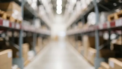 Blurred warehouse background featuring industrial metal shelving units and wooden pallets, providing a neutral backdrop suitable for commercial text overlays.