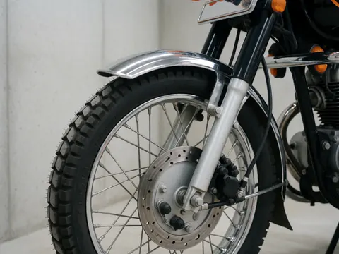 Macro shot of a mototaxi front wheel, suspension, tire, and chrome fender against a concrete wall.