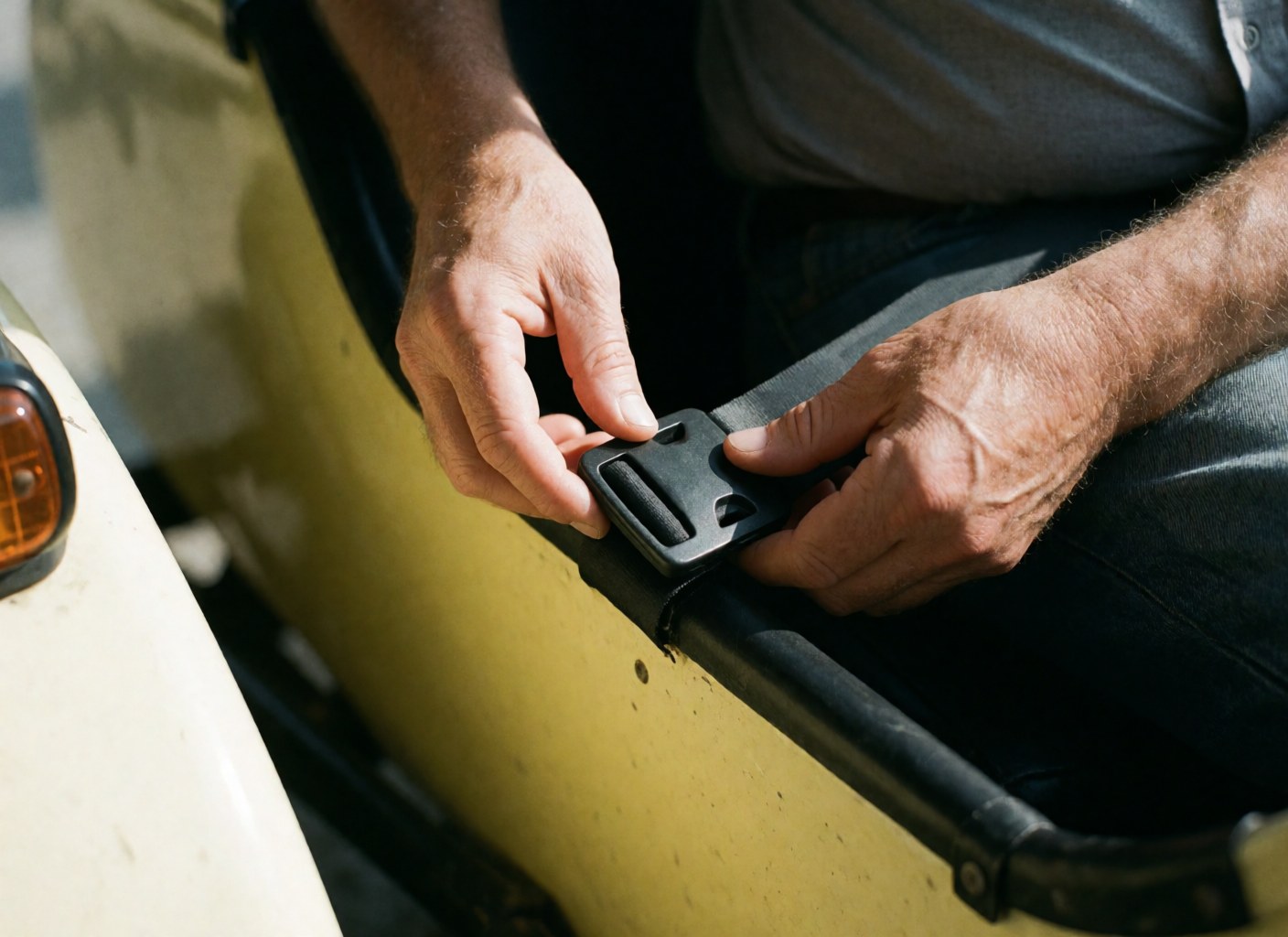 Close-up of hands fastening a seatbelt in a yellow sidecar, showing fabric and plastic textures under natural light