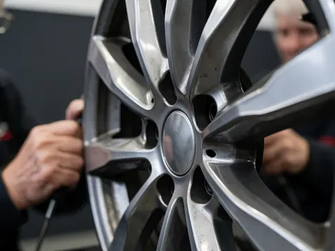 Close-up of mechanic hands adjusting an alloy wheel with spoke design in a gray-walled workshop