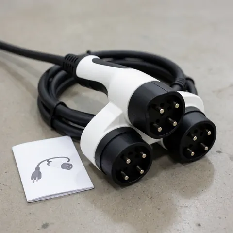 Universal charging adapter for electric vehicles featuring three connectors and a black cable resting on a concrete floor next to an illustrated manual.