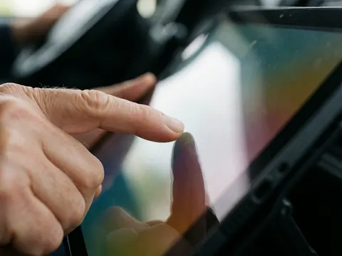 Close-up of fingers interacting with a digital control panel on a bus dashboard, featuring soft lighting and a blurred background.