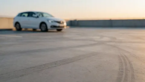 Blurred white car in background with warm sunset light and tire marks on concrete pavement