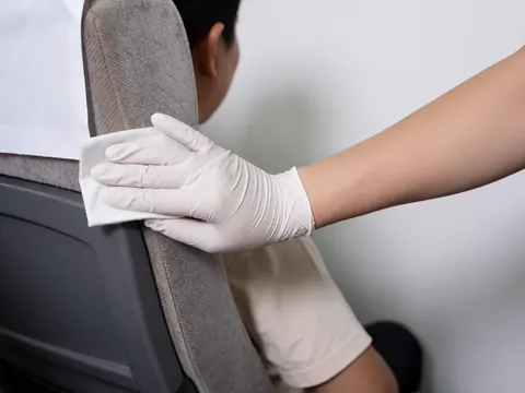 A gloved hand wipes a fabric bus seat with a disinfectant cloth to ensure hygiene and cleanliness for passengers.