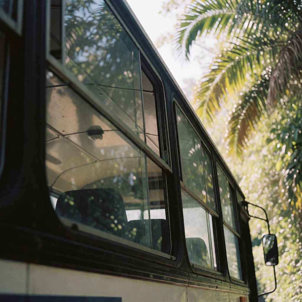 Exterior view of a tour bus featuring large windows and a sturdy chassis, surrounded by lush tropical foliage with filtered sunlight.