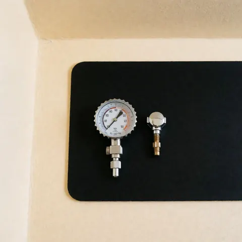 Black tire pressure gauge and valve cap placed on a black surface with a beige wall background for automotive maintenance