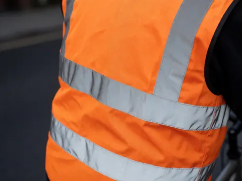 Close-up of an orange reflective vest with silver stripes, showing clean fabric texture and visible stitching details for bicycle taxi safety gear.