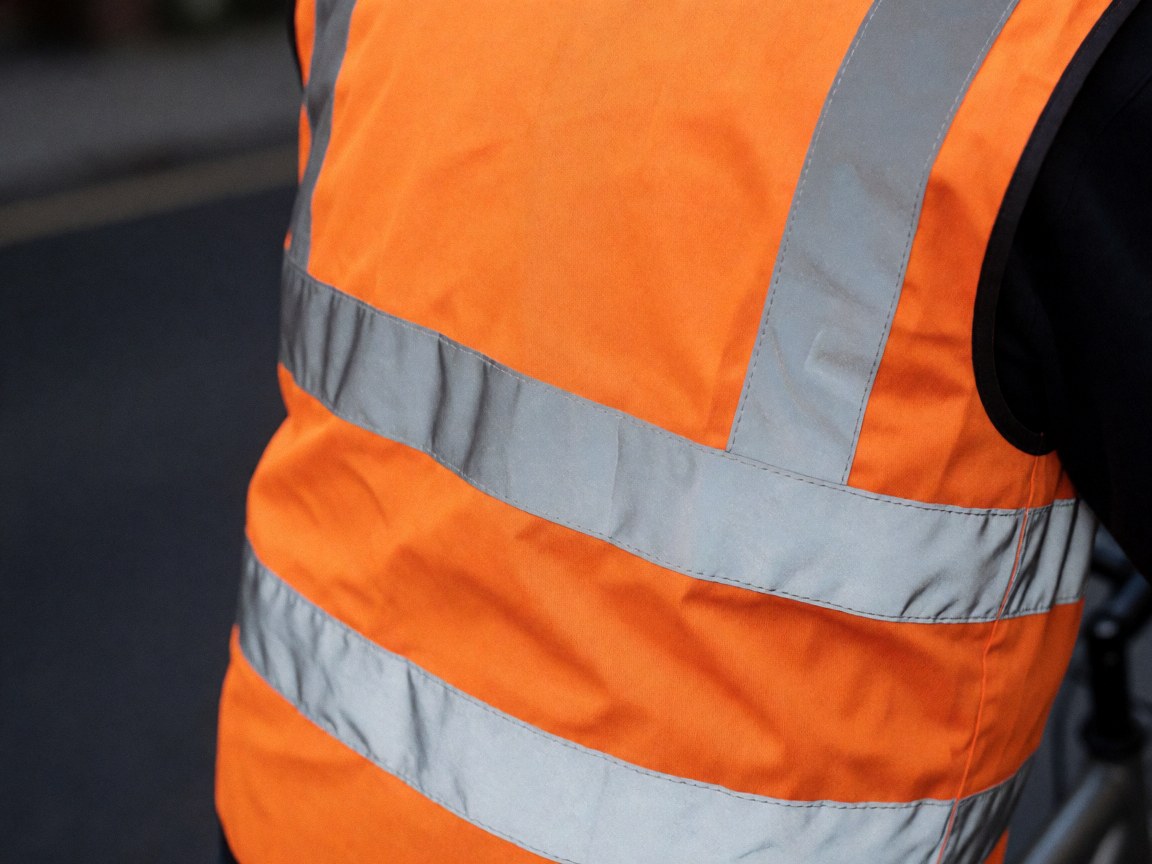 Close-up of an orange reflective vest with silver stripes, showing clean fabric texture and visible stitching details for bicycle taxi safety gear.