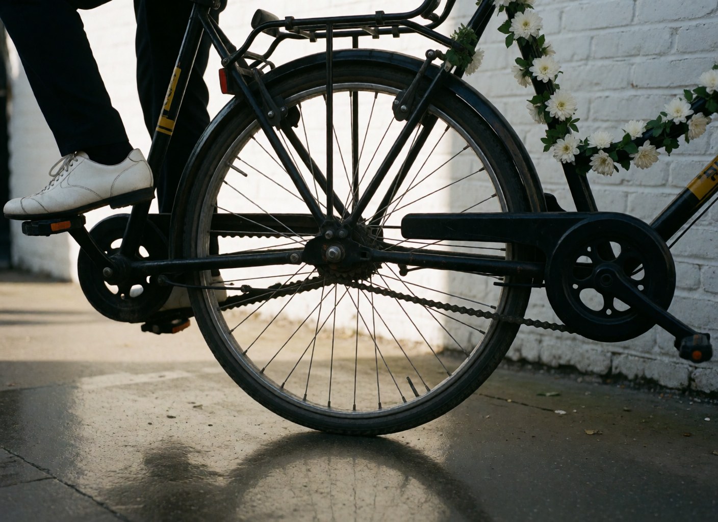 Close-up of a white shoe on the pedal of a black bicycle taxi decorated with white flowers near a white brick wall