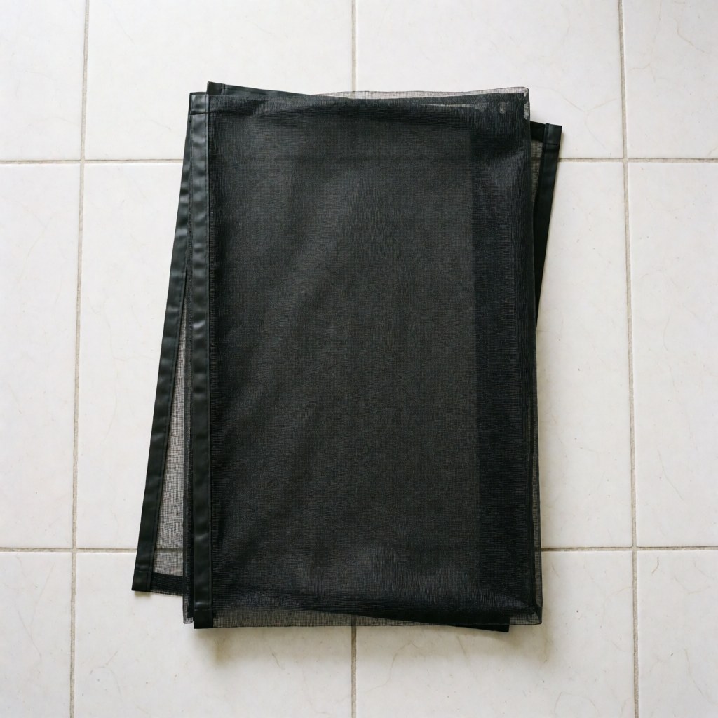 Folded black magnetic window screen with magnetic strips lying on white tiled floor ready for installation