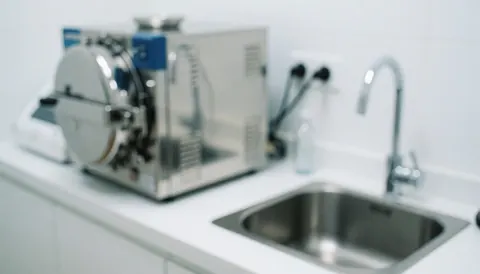 Sterile background featuring a metal autoclave and sink, ideal for tattoo studios. Clean surface with cool lighting and a professional atmosphere.