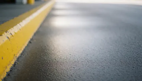 Yellow painted curb and wet asphalt surface with natural light reflections, serving as a professional background for commercial text overlays.